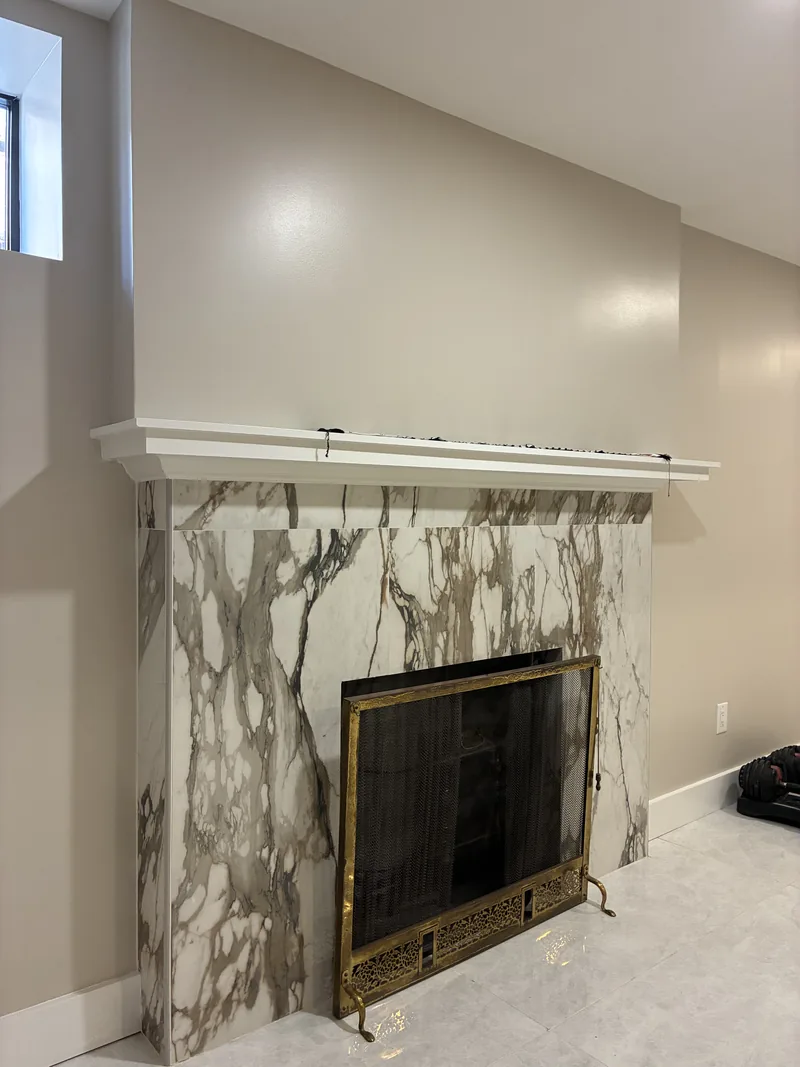 Living room fireplace with a heavily veined surround, white mantel, and black firebox.