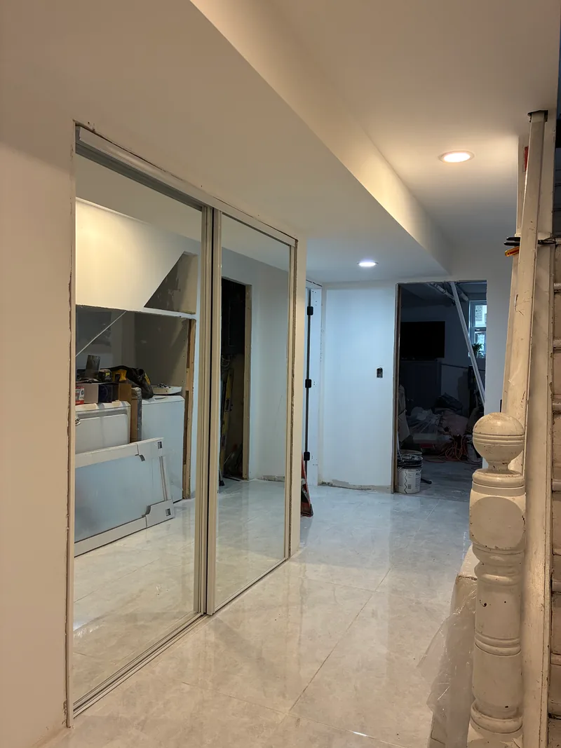 Renovated interior hallway with large-format tile flooring, mirrored sliding closet doors, white walls, and recessed ceiling lights.