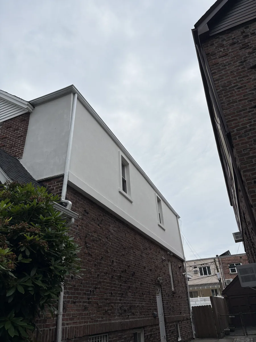 New rear addition with white stucco cladding, a finished roofline, and a single window, viewed from below.