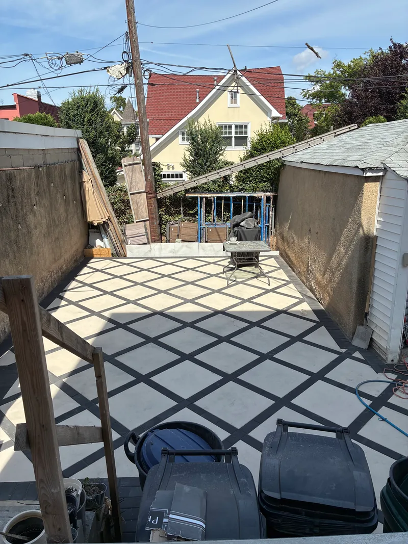 Rear patio under construction with a diamond-pattern concrete finish, freshly plastered perimeter walls, and materials at the edge of the work area.