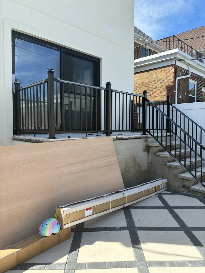 Rear entrance with new steps, black metal railings, and a tiled landing beside a sliding door.