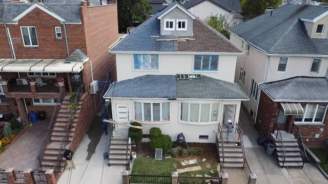 Two-story house with a new shingle roof, replacement windows, and an updated painted façade during an exterior renovation.