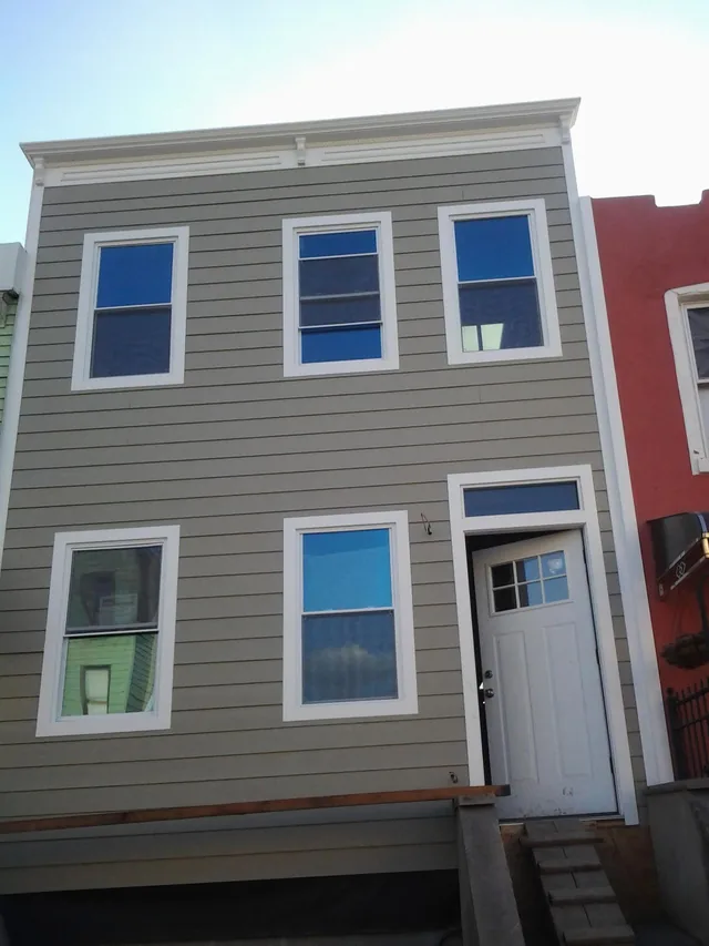 Two-story house with gray horizontal siding, white-trimmed windows, and a white entry door.