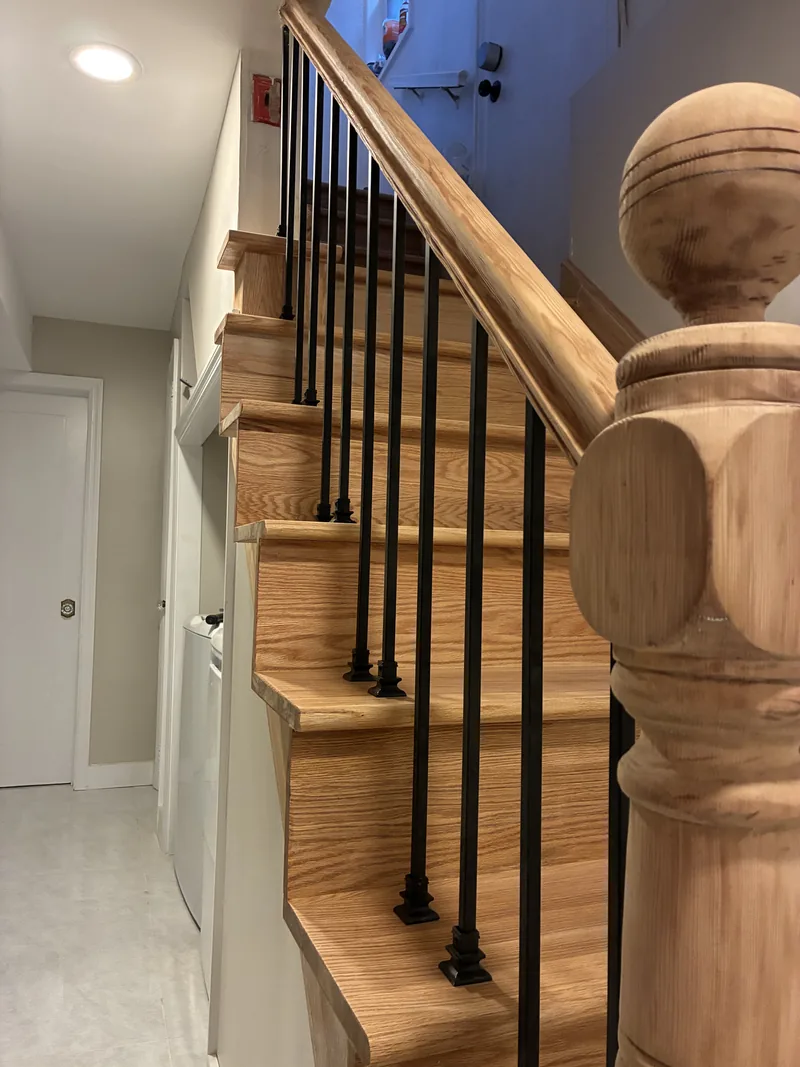 Close view of a wood staircase with a turned newel post, black metal balusters, and white risers.