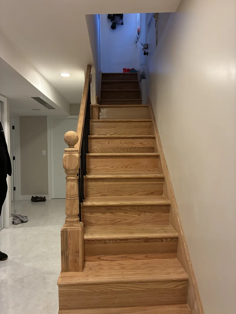 Finished wood staircase with wood treads, white risers, a wood handrail, and white walls.