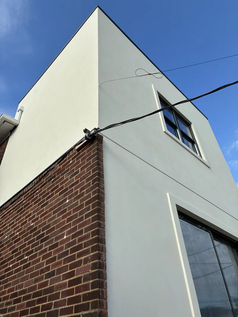 Exterior corner of a building with smooth white stucco above and a brick wall below, against a blue sky.