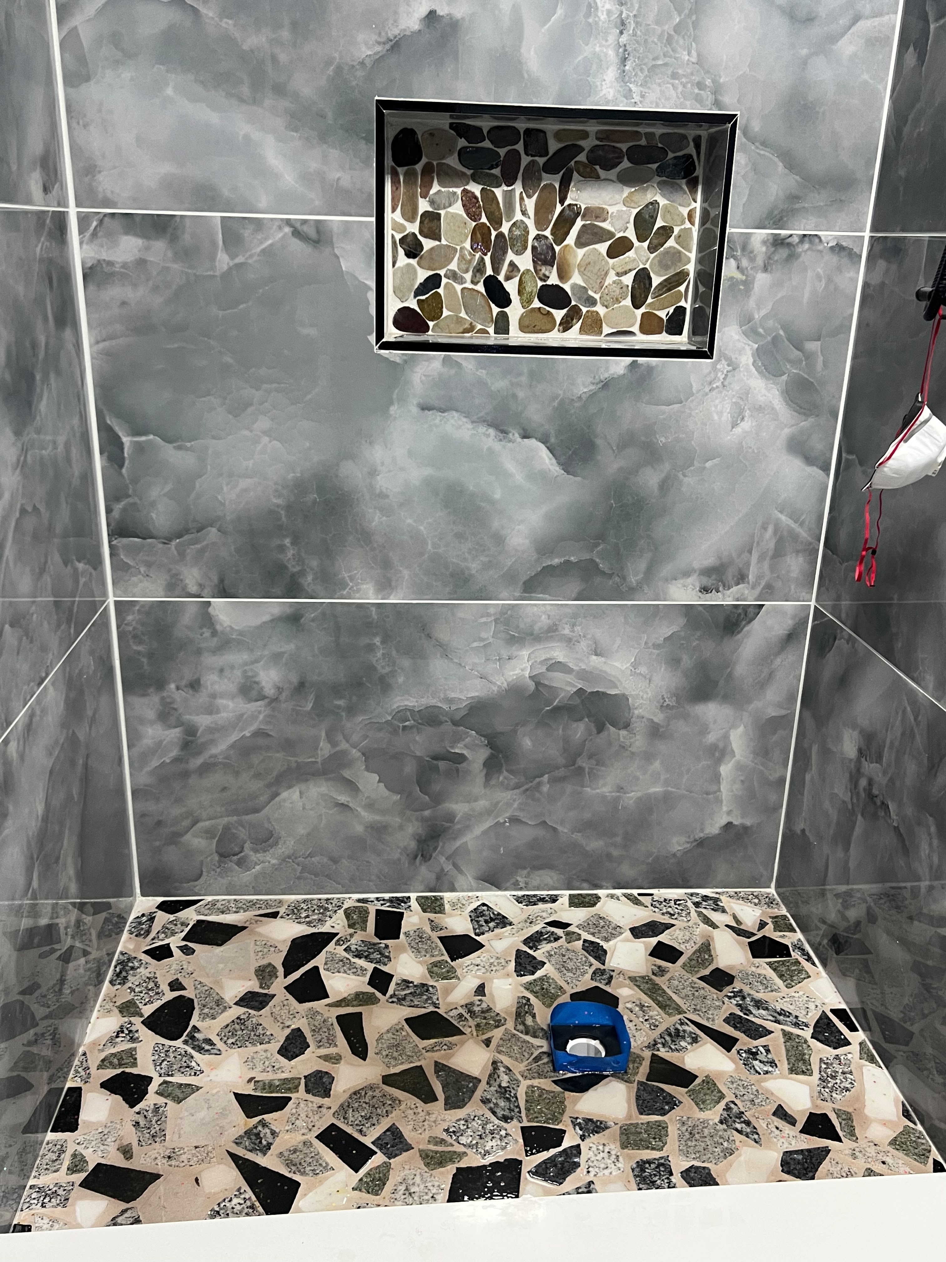 Shower wall in large gray stone-look tile with a framed pebble-tile niche and a matching pebble-tile floor.